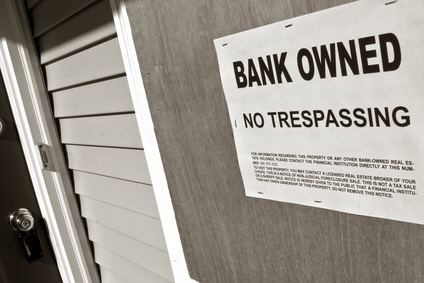 Bank owned sign posted on a boarded up house in Foreclosure