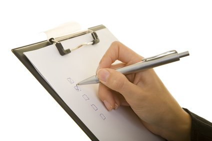 Hand mit Stift macht Häkchen auf einem Klemmbrett